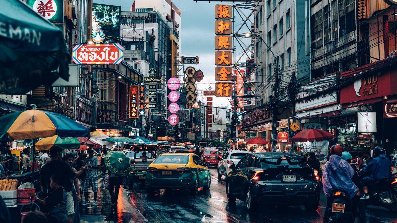 Bustling night market street scene in Bangkok, Thailand with neon signs and traffic.